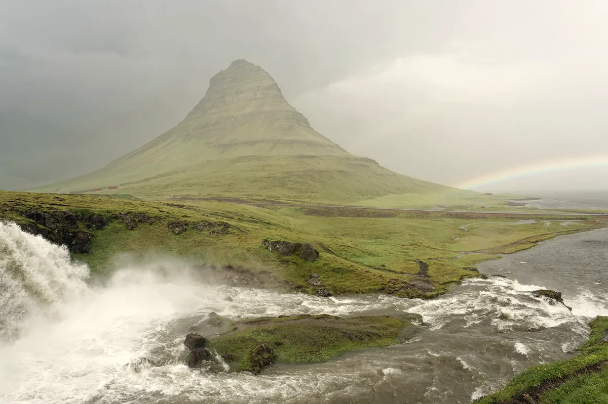 Kirkjufell mountain rising above green fields and a calm bay in west Iceland