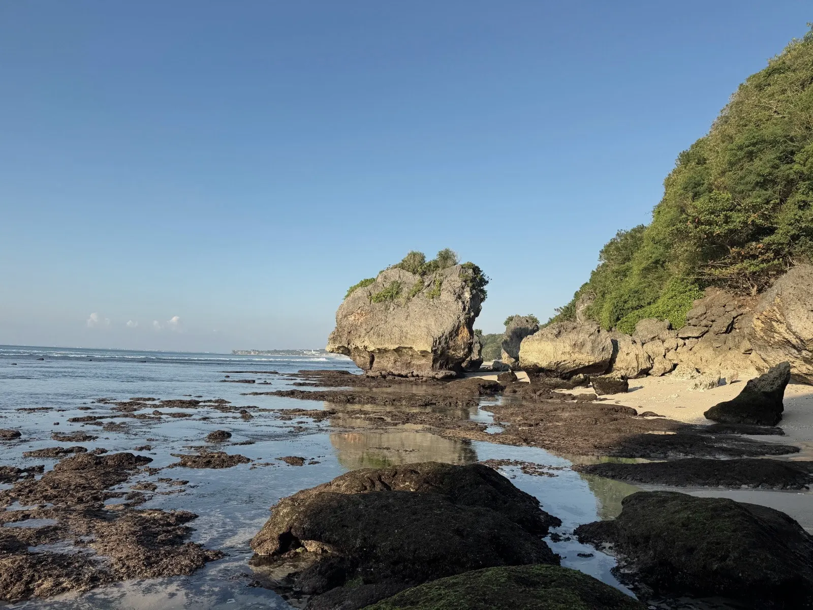 Calm low tide on a rocky beach below green cliffs near Uluwatu, Bali