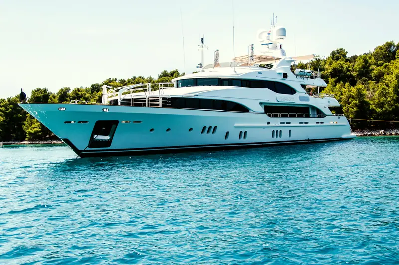 A small white yacht at anchor in a calm, green-walled cove, at sea