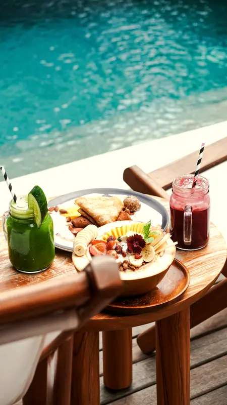 Green juice, beet juice and a fruit-topped coconut bowl beside a turquoise pool